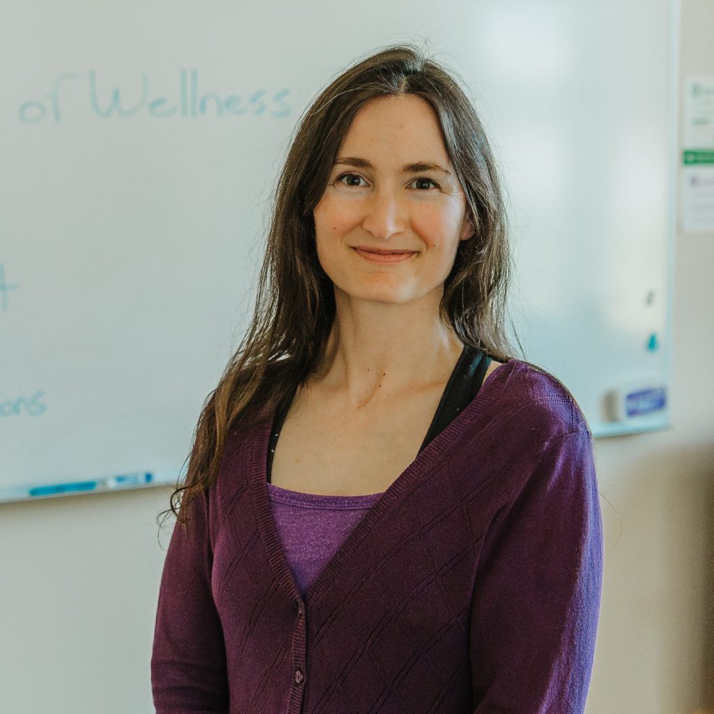 Sam Williams-Winslow smiling in front of whiteboard in yoga classroom
